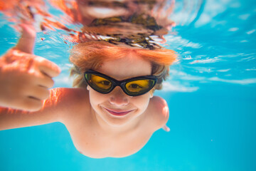 Naklejka premium Child in swimming pool underwater with thumbs up. Underwater kid swim in pool. Child boy swimming and diving underwater in pool. Summer family summer vacation with children. Underwater pool kids.