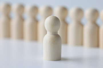 White wooden figure stands against blurred figurines in row