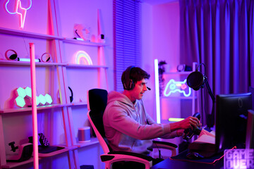 Caucasian handsome teen boy focus to use steering wheel for playing cyber sport racing car game...