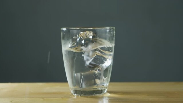 Ice cube dropping in to glass with water. B roll Slow motion 4k.