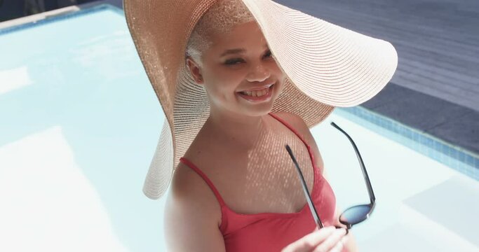 Portrait of happy biracial woman with sun hat at swimming pool in slow motion