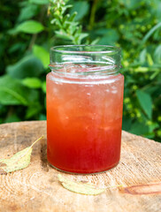 plan rpproché d'un verre au liquide rouge avec glace déposé sur une buche de bois fraîchement...