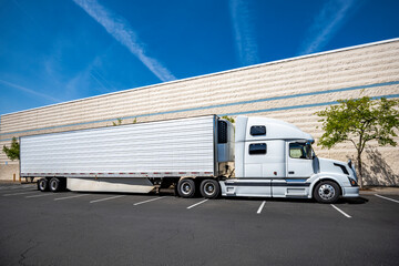 Bonnet white big rig industrial semi truck with refrigerator semi trailer standing on the warehouse...