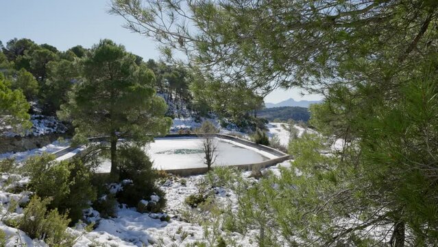 Snow-covered pine forest with a water reservoir in a sunny day in Sierra Mariola, Alicante, Spain, Mediterranean
