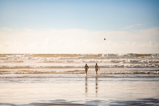 Couple of a man and a woman run to swim in the waves in the Northwest of the cold Pacific Ocean in the rays of the sun soluble in mist spray