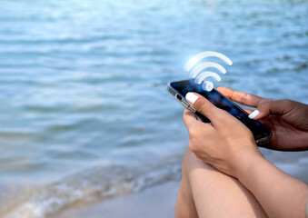 Wifi, 3d icon virtual on smart mobile phone. Wi-fi sharing symbol appear on cell phone holding by stylish female at the beach with sea and sand background with copy space. Social media lifestyle.