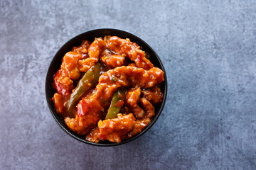 Schezwan Chicken or Dragon Chicken in black bowl at dark slate background. Szechuan Chicken is popular indo-chinese spicy dish with chilli peppers chicken and vegetables.