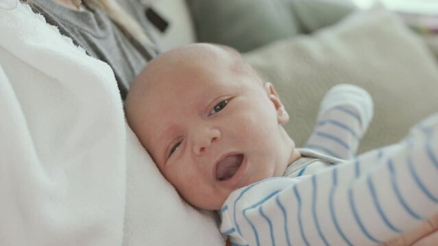 Newborn Baby in Held in Lap Being Moving Arms and Looking at Camera. slow motion side angle close up of an adult holding a newborn in her lap as the baby is swinging arms
