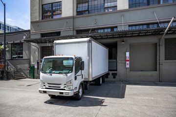 Small cabover rig semi truck with box trailer loading cargo standing in the warehouse dock on the...