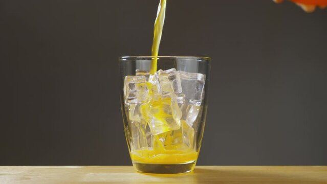 Orange soda is pouring into a glass with ice cube close-up on table. Orange soda. B roll Slow motion 4k.
