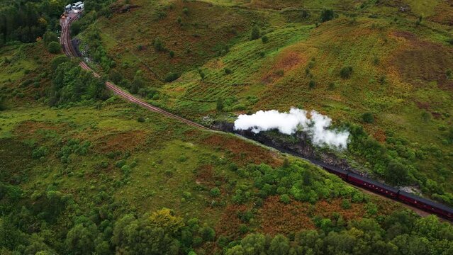 Aerial view following the Jacobite steam train on the West Highland Line, in cloudy Scotland