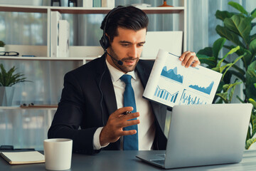Business man wearing headphone present financial data or BI paper via laptop during online meeting. Remote work concept with virtual meeting presentation of effectiveness remote work. Fervent