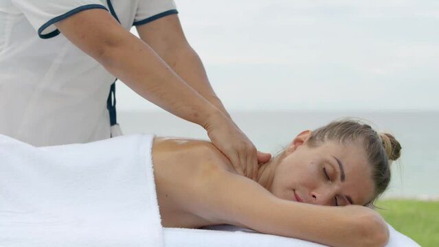 Woman reciving relaxing massage on special table on green grass, outdoor near the beach