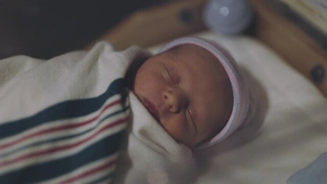 Newborn Baby in Hospital Crib. slow motion side angle close up of an infant newborn in a hospital crib swaddled sleeping with a cap