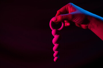 Woman holding anal beads in neon pink blue light. Copy space. 