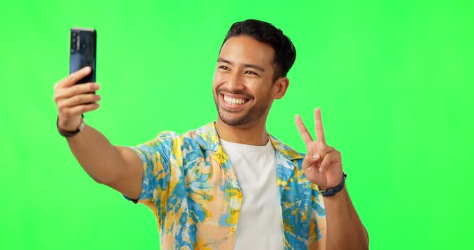 Selfie, man and peace sign in green screen studio, happy and excited on mockup background. Social media, photo and asian male influencer with peaceful emoji smile for profile picture, blog or pose