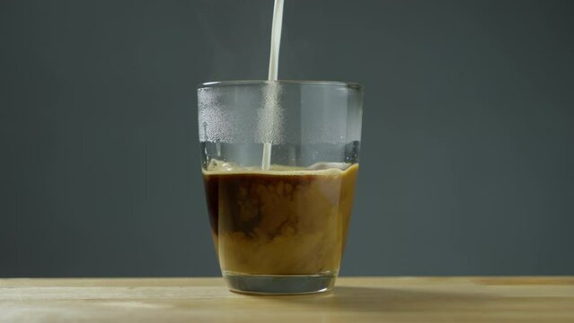 Milk poured into a transparent cup of coffee. Americano coffee with pouring milk. B roll Slow motion 4k.