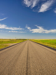 Vertical image of the flat expanse of farmland and the straight and narrow highway through the plains of Saskatchewan Canada - 605548282