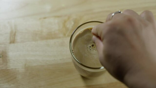 Top view of Person hand steering coffee in a cup with spoon. Breakfast morning of a cup hot black coffee on wooden background. footage b-roll scene 4k. home making coffee.