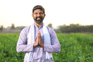 Happy rural Indian bearded farmer standing in his flourished field with his hands folded , joined 