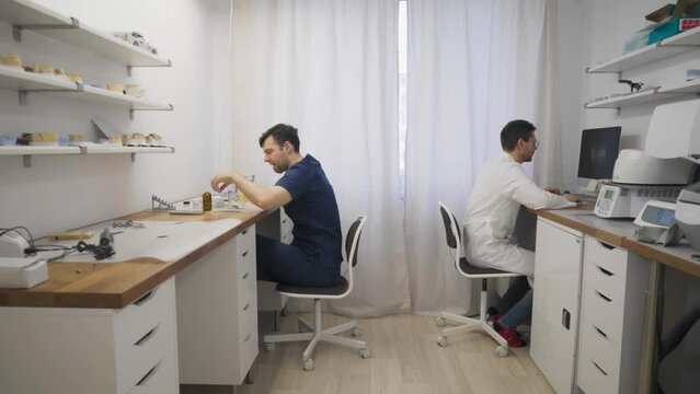 Technicians are creating prosthetic dental implants at the laboratory. Technician is assembling the teeth models at the dental laboratory. Technician is examining the 3D dental model at the lab