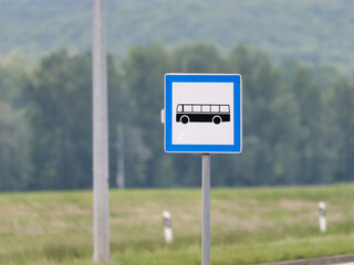 Close-up photo of a Bus Stop Sign on a metal pole with the trees in the background