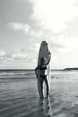 Fototapeta na wymiar Surfing, Girl surfer with a longboard on the beach of Weligama, Indian Ocean Active water sports, travel, surf school, surf camps. Active lifestyle,bw, black and white, monochrome