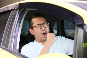 Adult Asian man yawning when driving his car