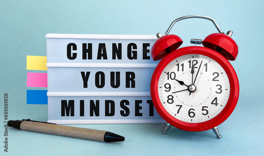 Poster text change your mindset written on the lightbox with alarm clock and colorfull stickers on blue bac