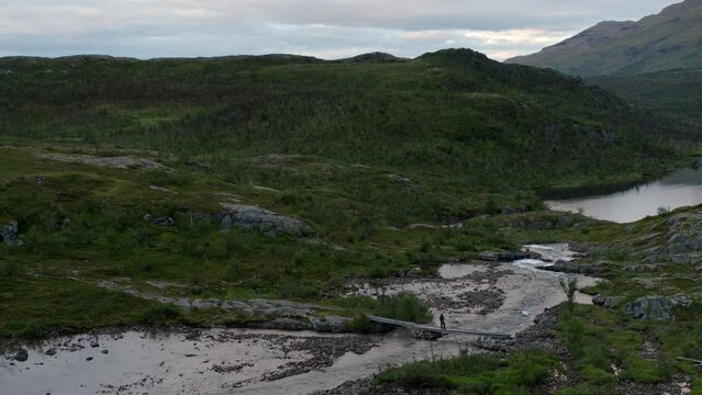 Unrecognizable man fishing in stream by green hills in Sweden, aerial