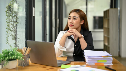 Thoughtful female accountant is looking out the window, daydreaming