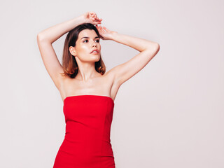 Fototapeta premium Young beautiful smiling female in trendy summer red evening dress. Sexy carefree brunette woman posing in studio, isolated on white. Positive model with evening makeup. Cheerful and happy