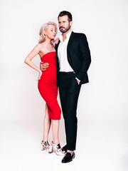 Beautiful fashion woman and her handsome boyfriend in black elegant suit. Sexy blond model in red evening dress. Fashionable couple posing in studio. Brutal man and his female. Isolated on white