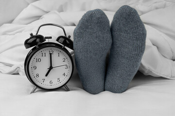 Alarm clock on bed next to female feet in socks