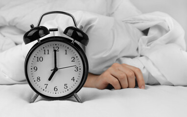 Woman's hand lying near black alarm clock on bed
