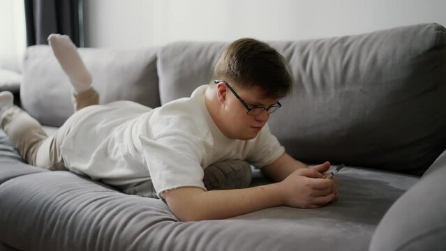 Young man with down syndrome using cellphone while resting on couch at home