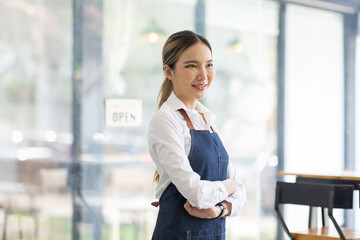 Asian Happy business woman is a waitress in an apron, the owner of the cafe stands at the door with a sign Open waiting for customers , cafes and restaurants Small business concept.
