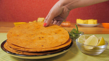 Beautiful hands of a female picking up a Khakra from a plate kept on the  mat. Popular Gujarati breakfast Khakra served with fresh green chilies and sliced lemon against a blurred background