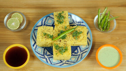 Woman's beautiful hands keeping a fresh green chilly on a plate of khaman Dhokla. Closeup shot of...
