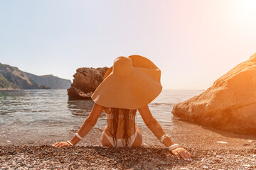 woman sea travel Tanned middle-aged woman with long hair and a white bathing suit. He sits on the seashore in a large sun hat with his back and looks at the sea.