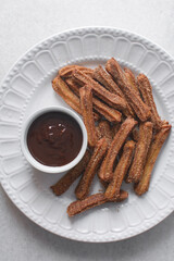 Top view of cinnamon sugar covered churros in a white plate with chocolate sauce in a ramekin, Fried churros in a plate