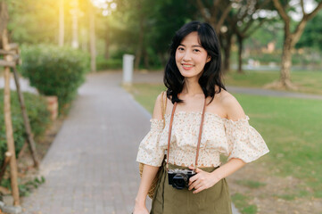 Portrait of asian young woman traveler with weaving hat and basket and a camera on green public park nature background. Journey trip lifestyle, world travel explorer or Asia summer tourism concept.