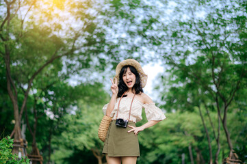 Portrait of asian young woman traveler with weaving hat and basket and a camera on green public park nature background. Journey trip lifestyle, world travel explorer or Asia summer tourism concept.