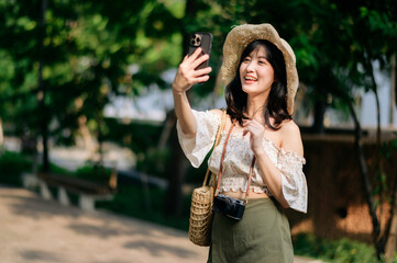 Portrait of asian young woman traveler with weaving hat, basket, mobile phone and camera on green public park background. Journey trip lifestyle, world travel explorer or Asia summer tourism concept.