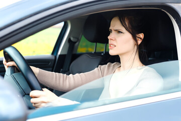 An angry girl grips the steering wheel tightly, frustration evident in her eyes. Stuck in slow traffic, she yearns to break free and escape the ceaseless crawl of cars.