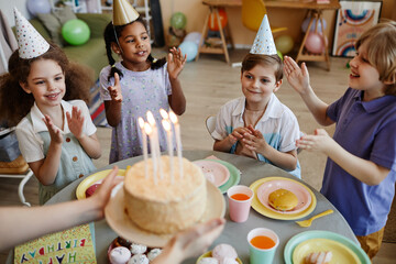 High angle view at diverse group of happy children clapping while waiting for cake with candles...