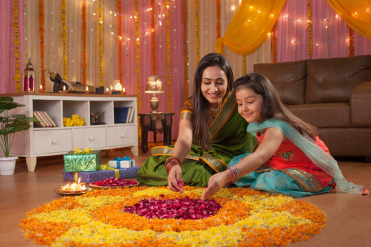 Beautiful mother and daughter making rangoli on diwali festival - Colorful background. Image of mother and daughter putting rose petals in rangoli on occasion of diwali. Posing for the camera with ...