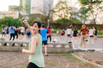 Obraz premium Female jogger. Fit young Asian woman with green sportswear aerobics dance exercise in park and enjoying a healthy outdoor. Fitness runner girl in public park. Wellness being concept