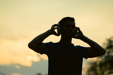 Silhouettes of male runner wearing headphone, standing under golden sunset sky in evening time