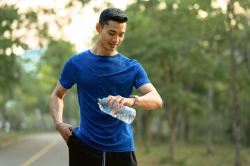 Fototapeta premium Happy sportsman with bottle of water checking smartwatch to monitor training results. Technology health, wellness concept